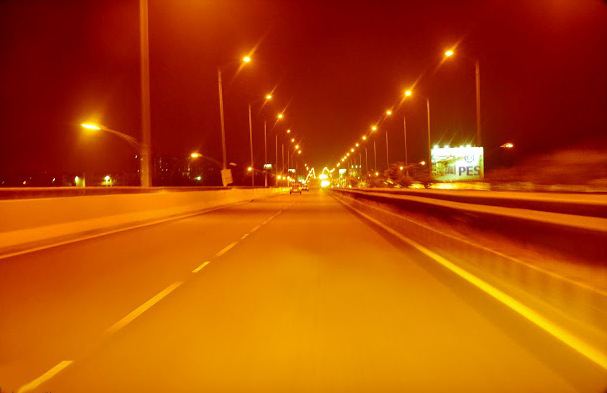 The elevated expressway at night, sodium lamps burning orange down its length