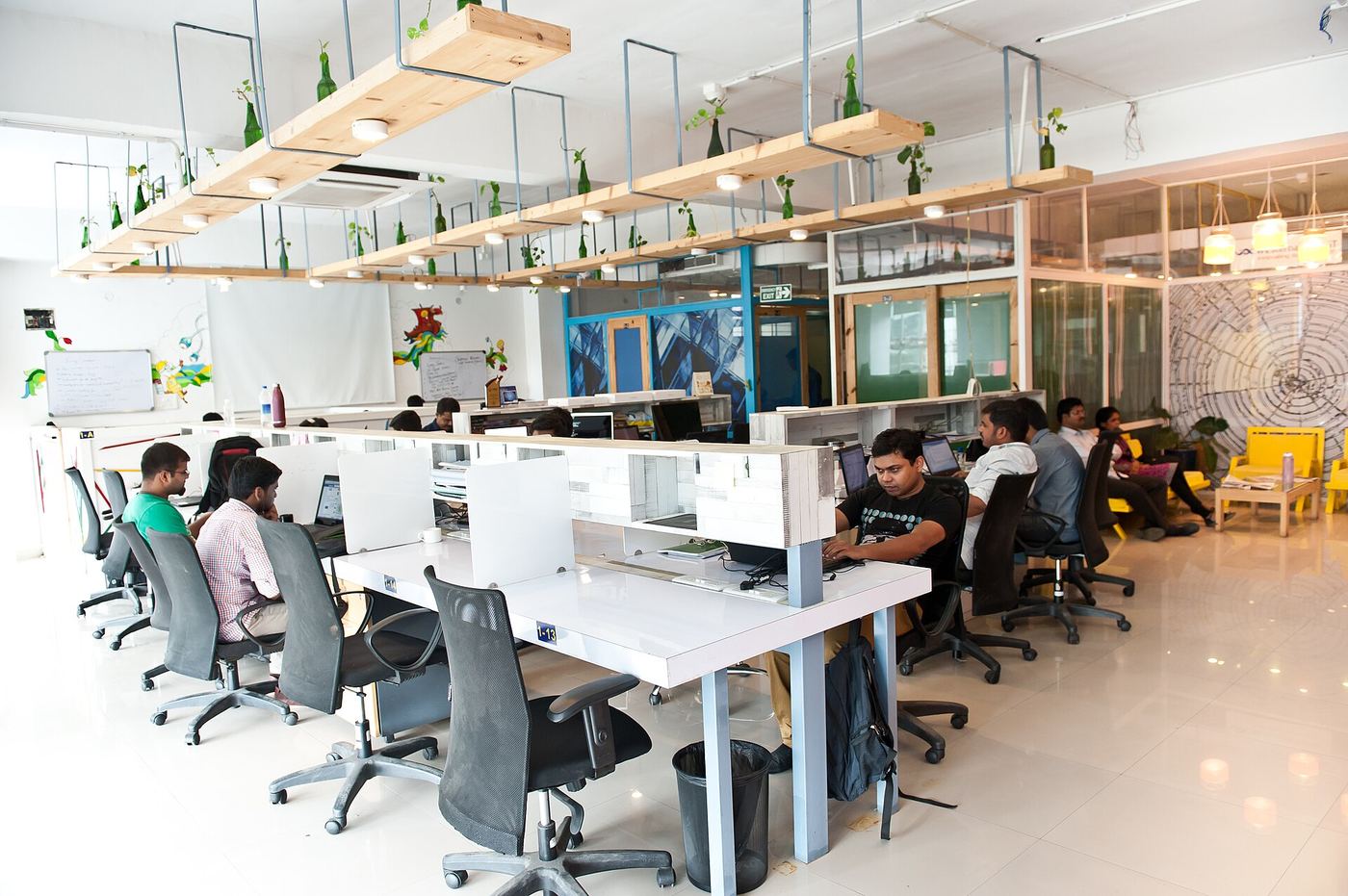 A bright coworking floor with long shared desks and hanging plants