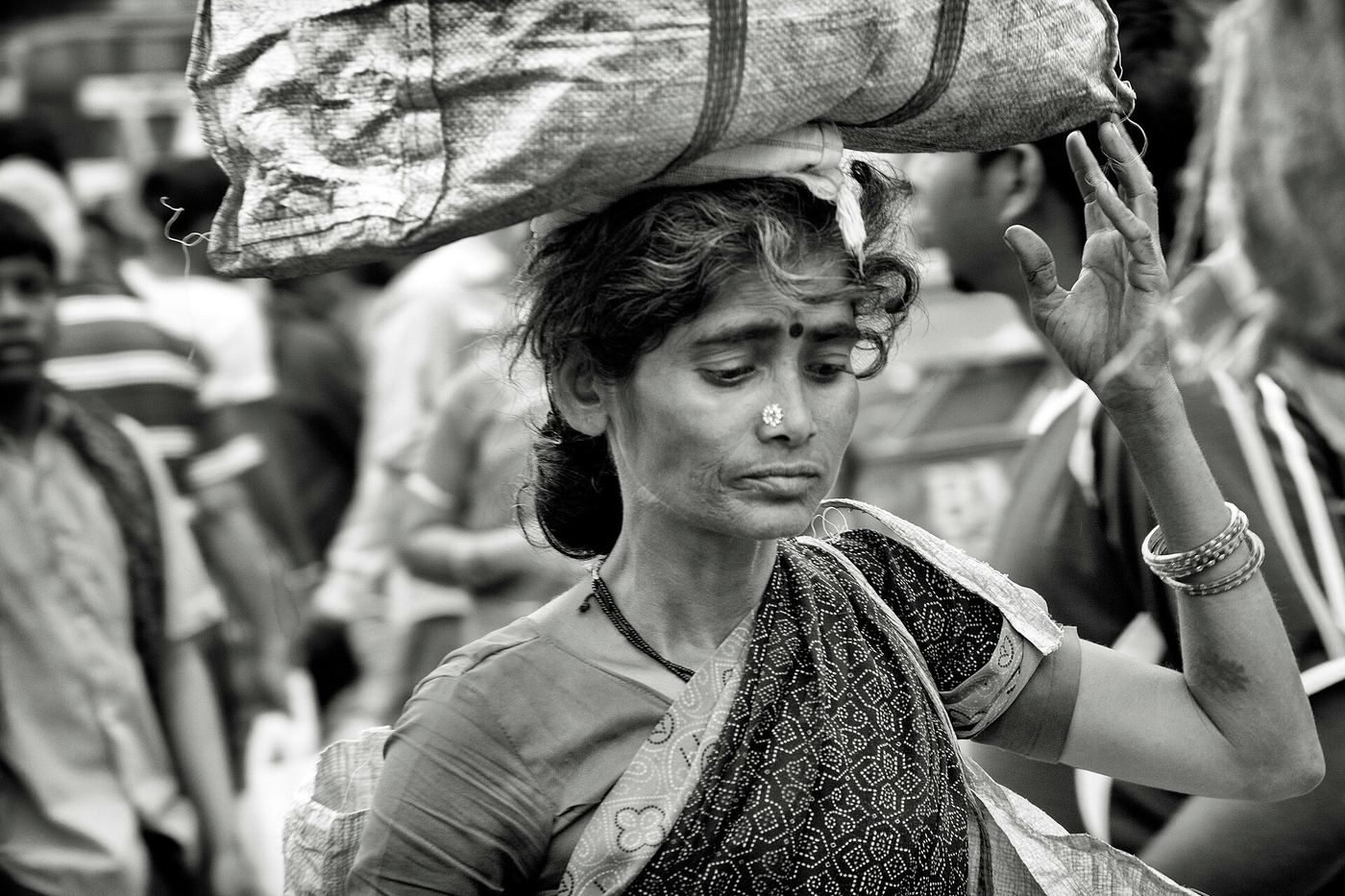 A woman carries a heavy bundle on her head through the crowded City Market